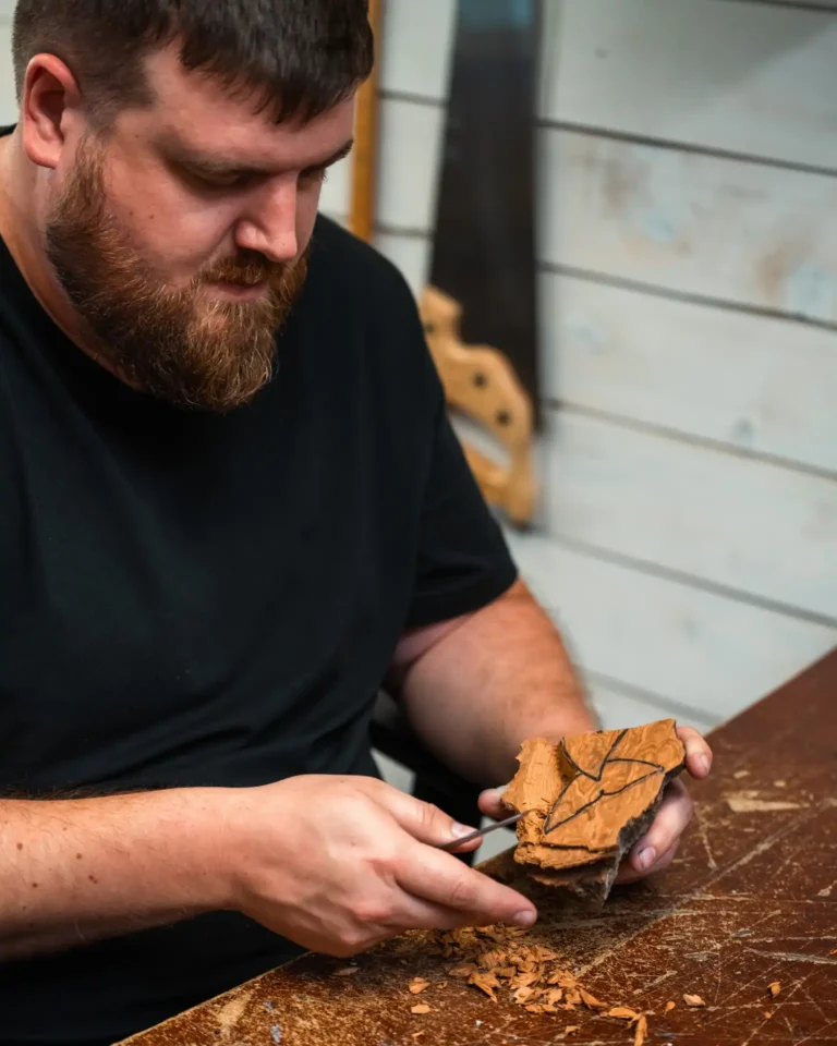 Nathan Keil hand-carving a wooden whale tail sculpture at Come From Away Carvings’ studio.