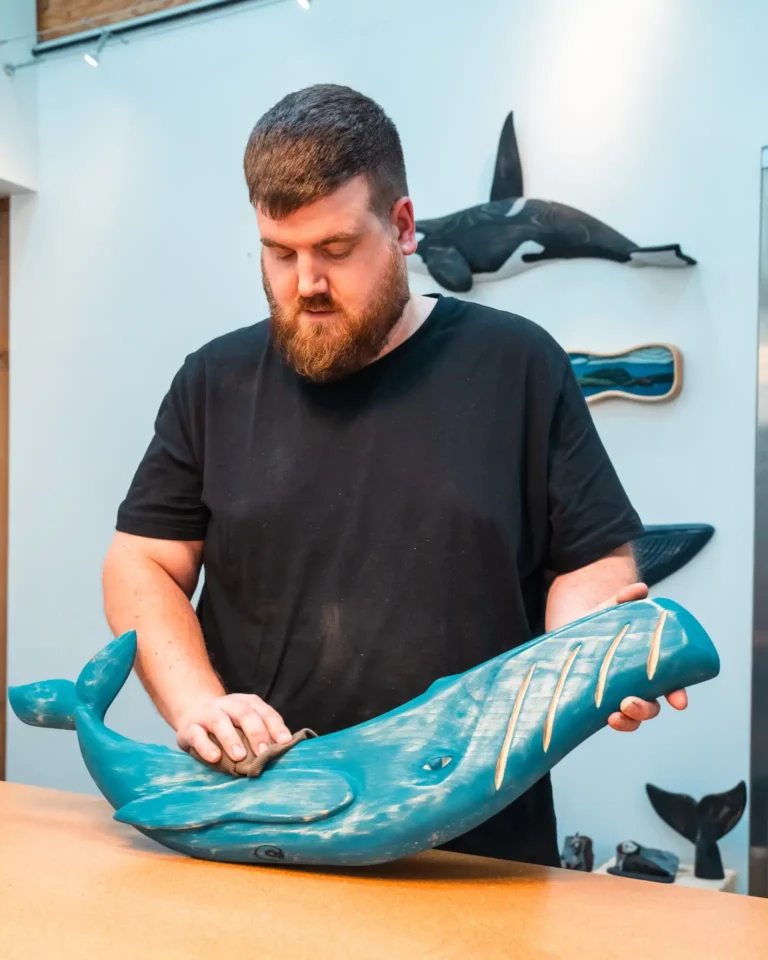 Nathan Keil holding a blue whale sculpture with more whale art mounted on the wall behind.